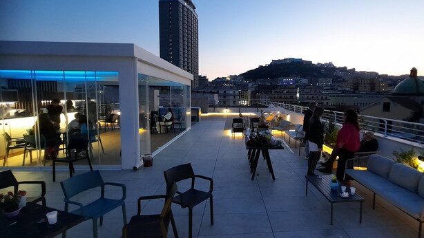 A rooftop terrace with outdoor seating, a glass-enclosed area, and a cityscape view in the background. - Napolinn B&B (Naples)
