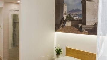 Un dormitorio con una cama, aire acondicionado instalado en la pared, una planta en maceta y vista a un paisaje urbano a través de un arco.