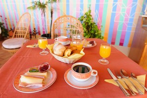 A breakfast table set with plates of food, a basket of bread, a jug of orange juice, and a cup of coffee. - Welwitshia guest house (Lagoa)
