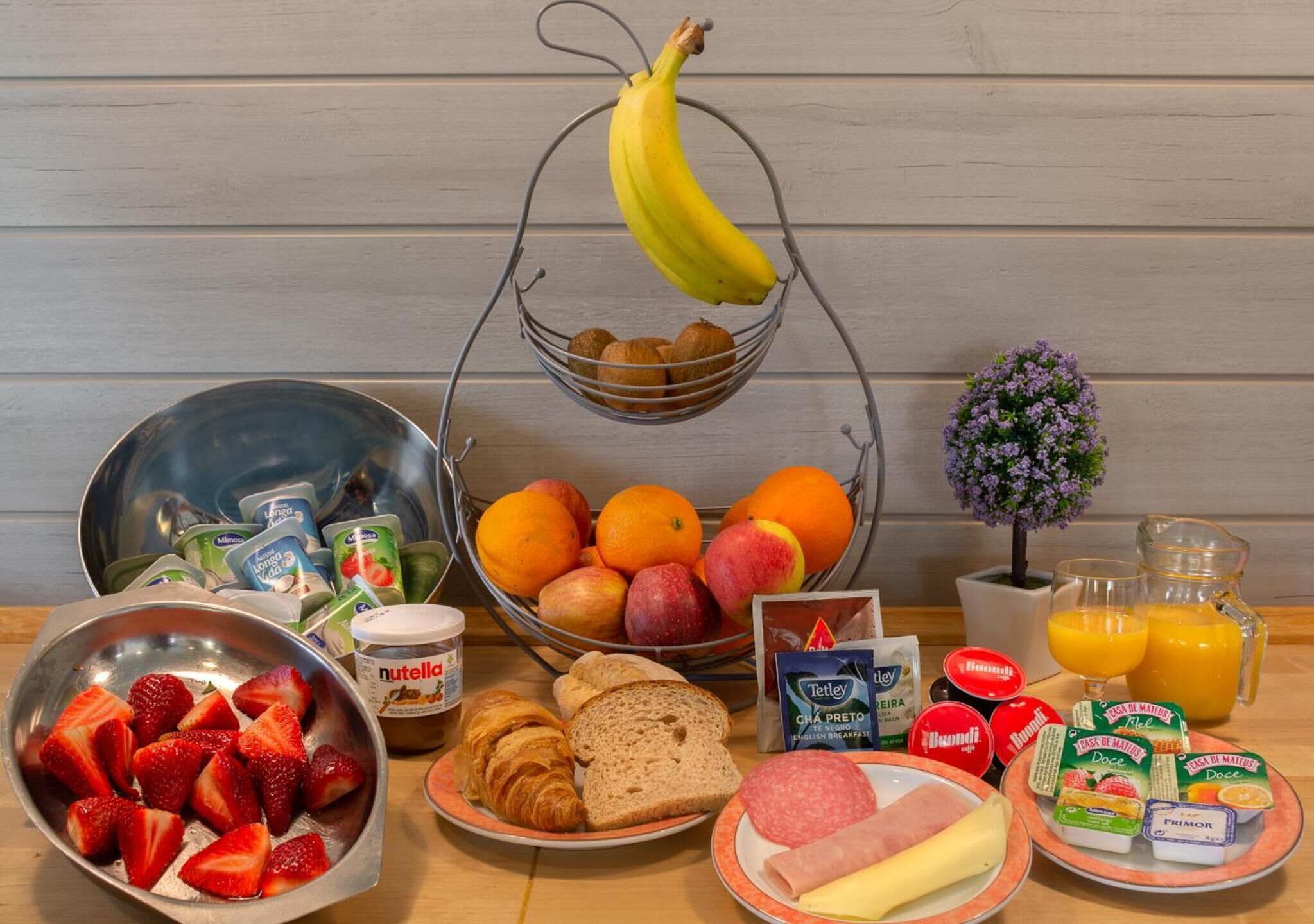 A breakfast table with various food items including fruits, bread, cheese, and condiments.