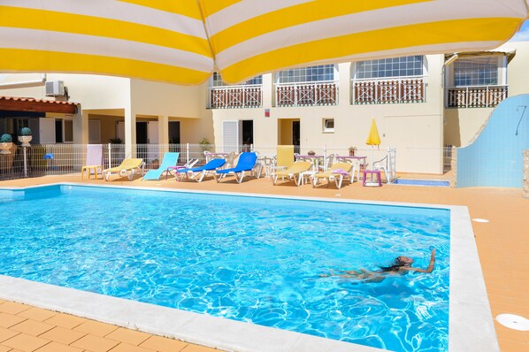 An indoor swimming pool with lounge chairs and umbrellas, surrounded by a white and yellow striped canopy.