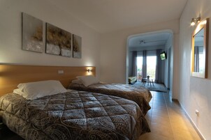 Habitación de hotel con dos camas, cabecero de madera y vista a un balcón.