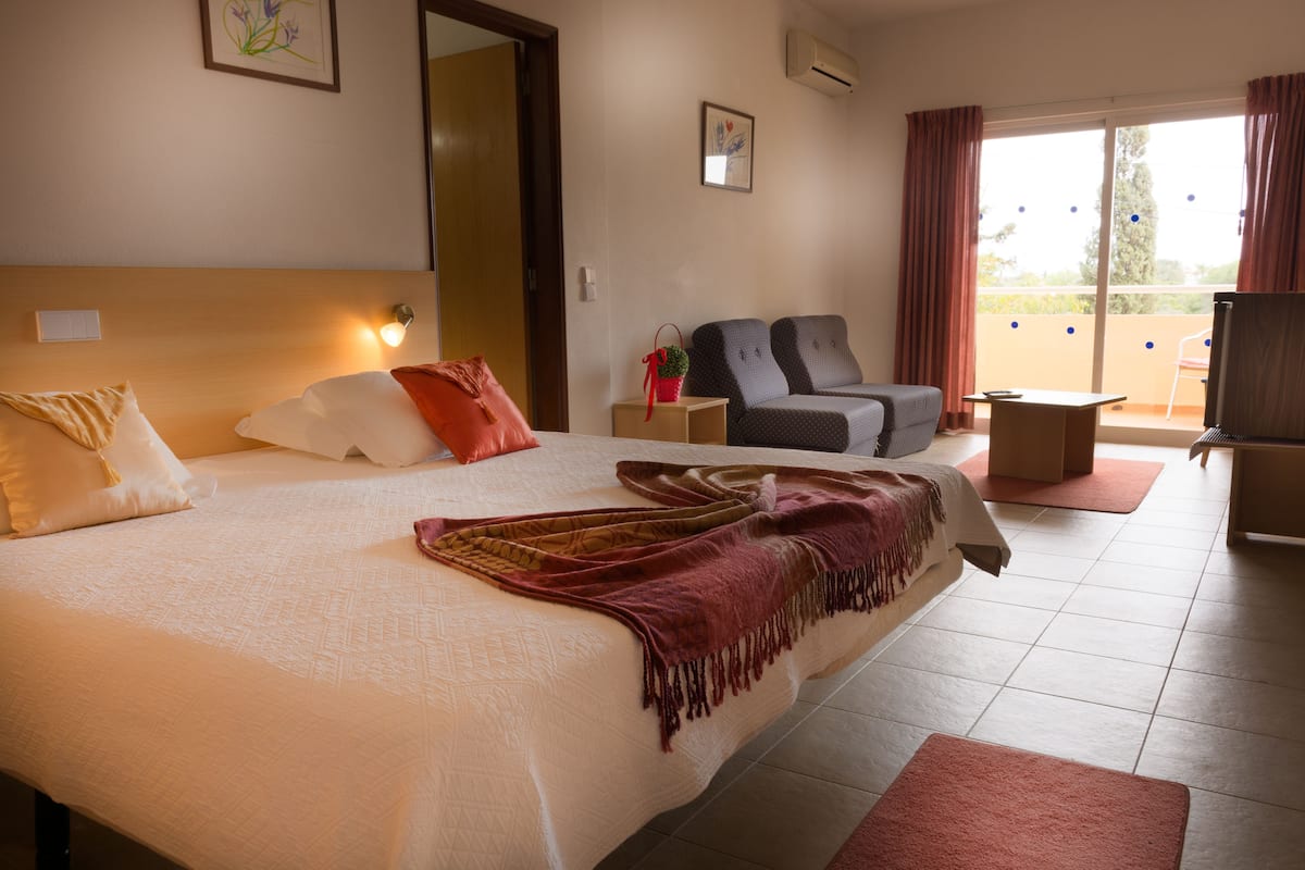 A hotel room with a large bed, a desk, a chair, and a balcony with a view.