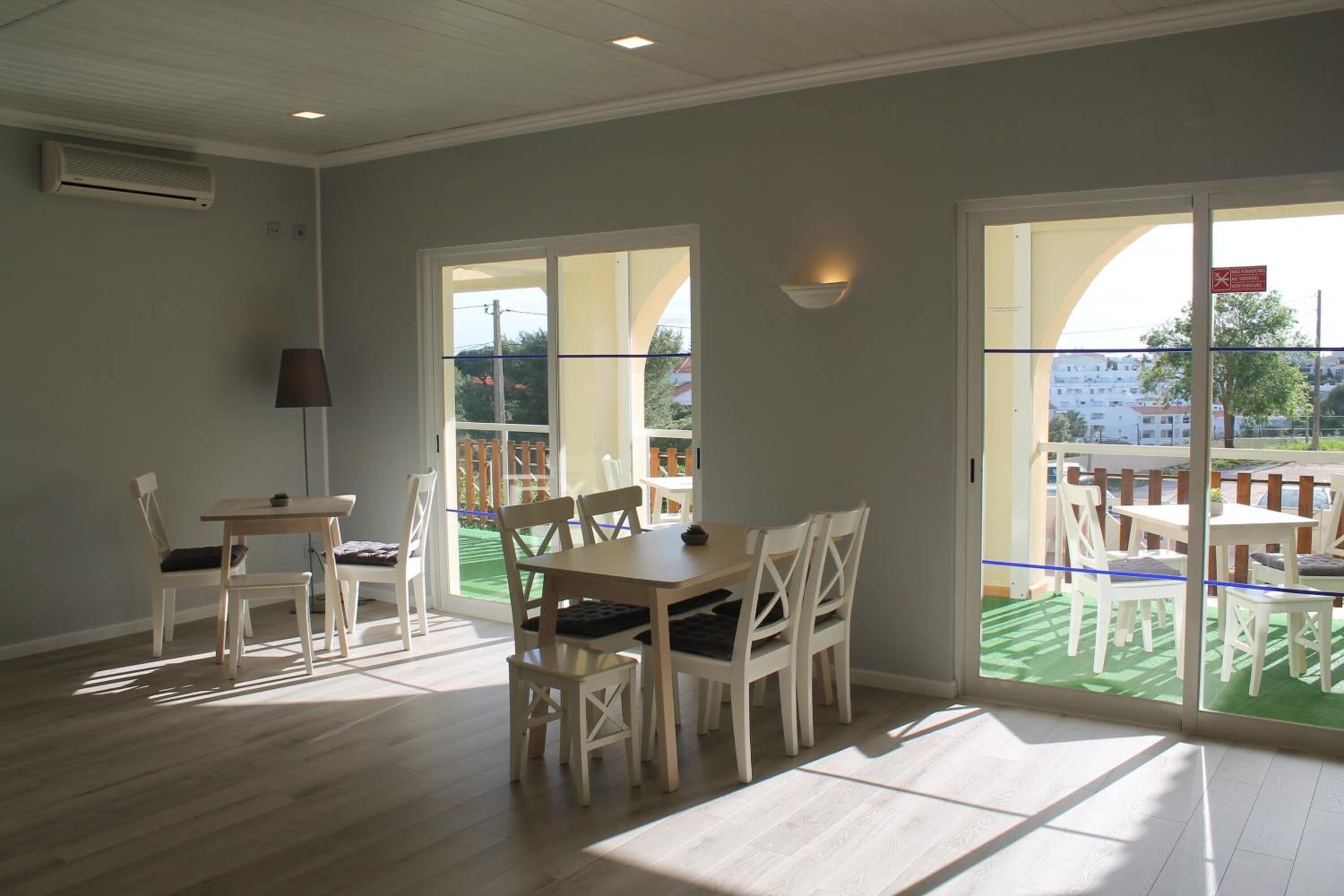 A room with a dining table and chairs, a lamp, and a view of an outdoor area with tables and chairs.