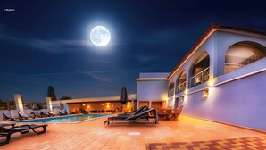 Un espace piscine avec des chaises longues et une lune dans le ciel.