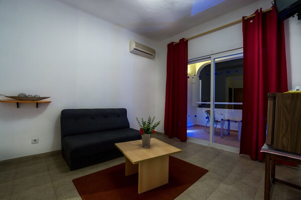 A living room with a sofa, a small table with a vase, and a sliding glass door leading to an outdoor area. - Welwitshia guest house (Lagoa)