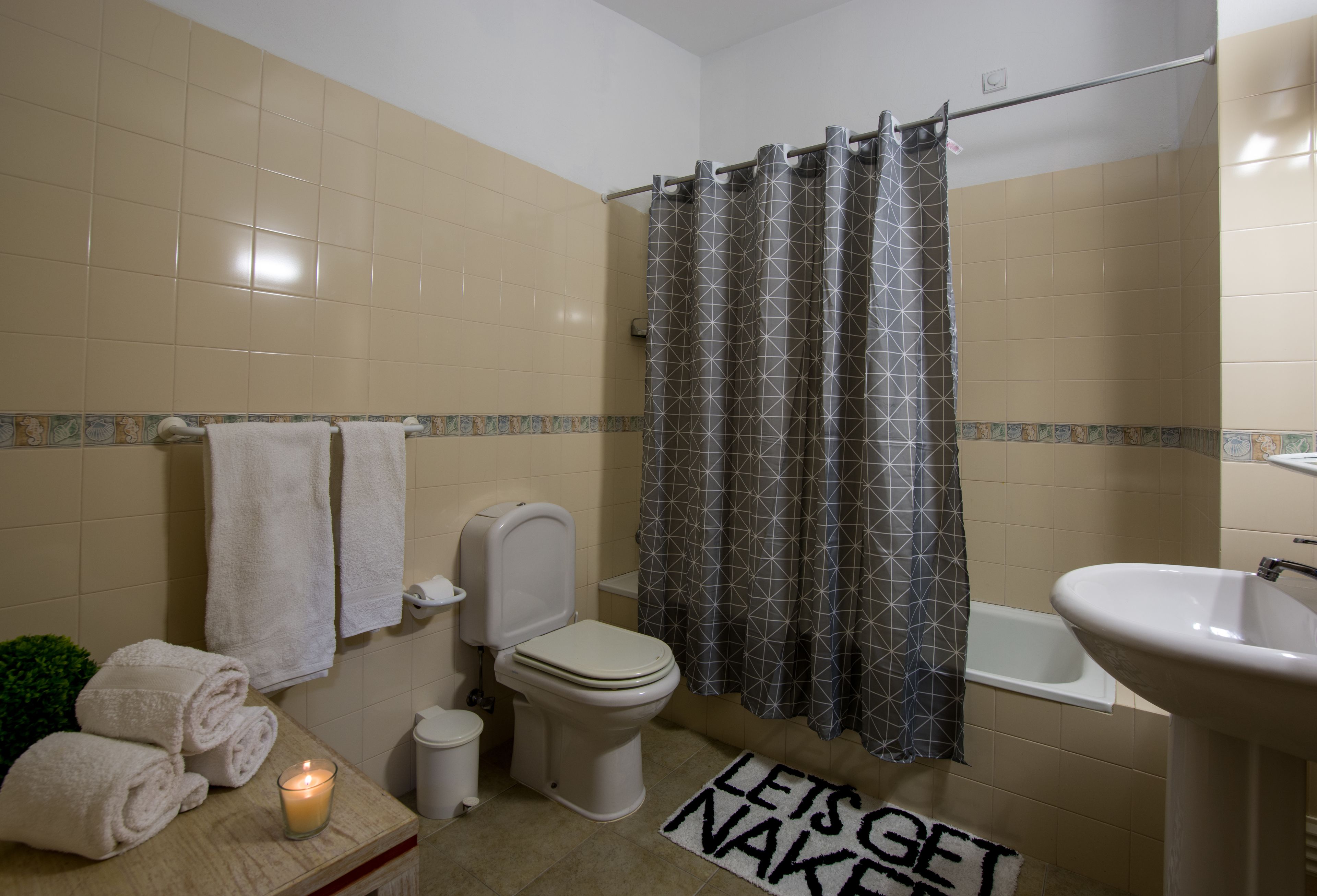 A bathroom with a toilet, sink, and shower curtain. There are towels and a candle on the counter.