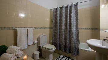 A bathroom with a toilet, sink, and shower curtain. There are towels and a candle on the counter.