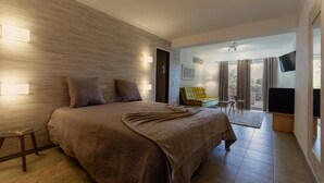 Une chambre avec un grand lit, une petite table, une chaise, une télévision et un balcon avec des rideaux.