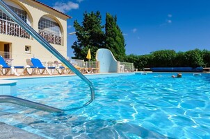 Una piscina con agua azul cristalina, un trampolín y sillas de descanso.