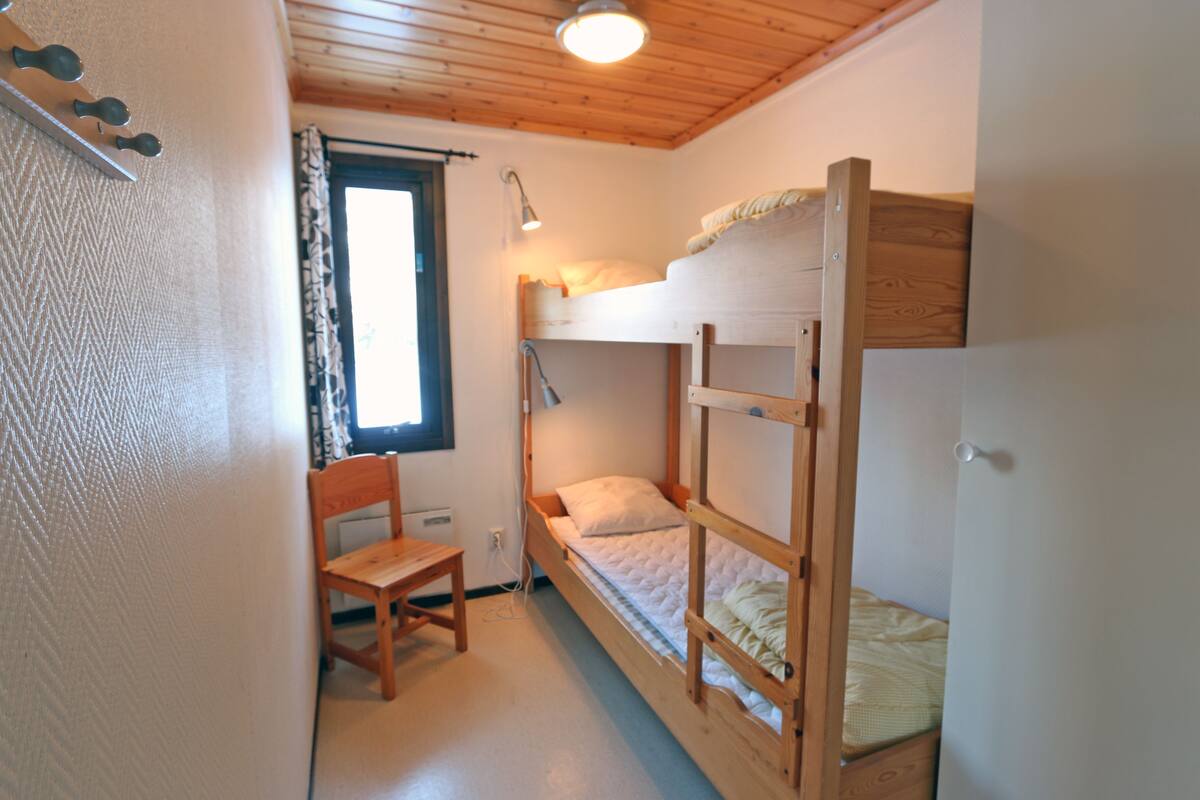 Eine einfache, kleine Unterkunft mit einem Schlafstockbett, einem Holzbett, einem Schreibtisch und einem Fenster mit Vorhängen.