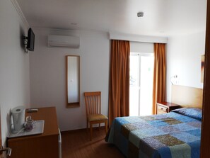 A hotel room with a bed, a chair, a desk with a coffee maker, a mirror, and a window with curtains.