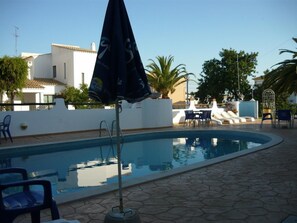 A swimming pool with lounge chairs and umbrellas, surrounded by a white wall and potted plants.