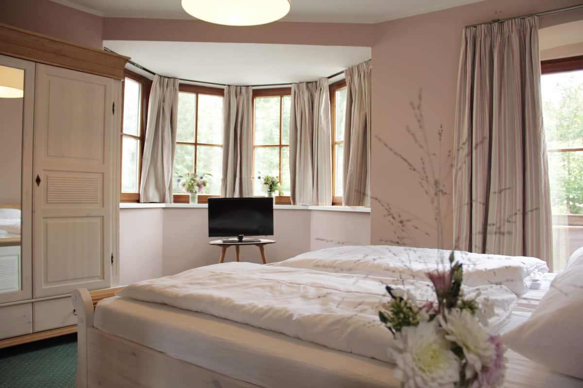 A bedroom with two beds, a television on a small table, and large windows with curtains.