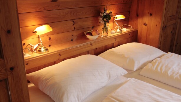 Una habitación tipo cabaña de madera con dos camas, una mesita de noche con lámparas, un cuenco de fruta y un florero con flores.
