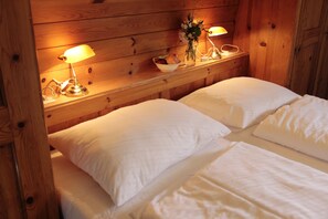 Une pièce aménagée comme un chalet en bois, avec deux lits, une table de chevet avec des lampes, un panier de fruits et un vase rempli de fleurs.