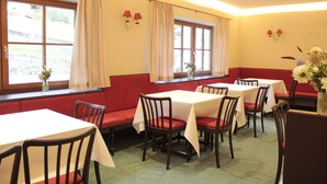 Un restaurante con cabinas y mesas, asientos acolchados en rojo y ventanas con cortinas.