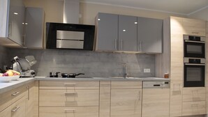 Una cocina moderna con armarios de madera clara, electrodomésticos de acero inoxidable y encimera gris.