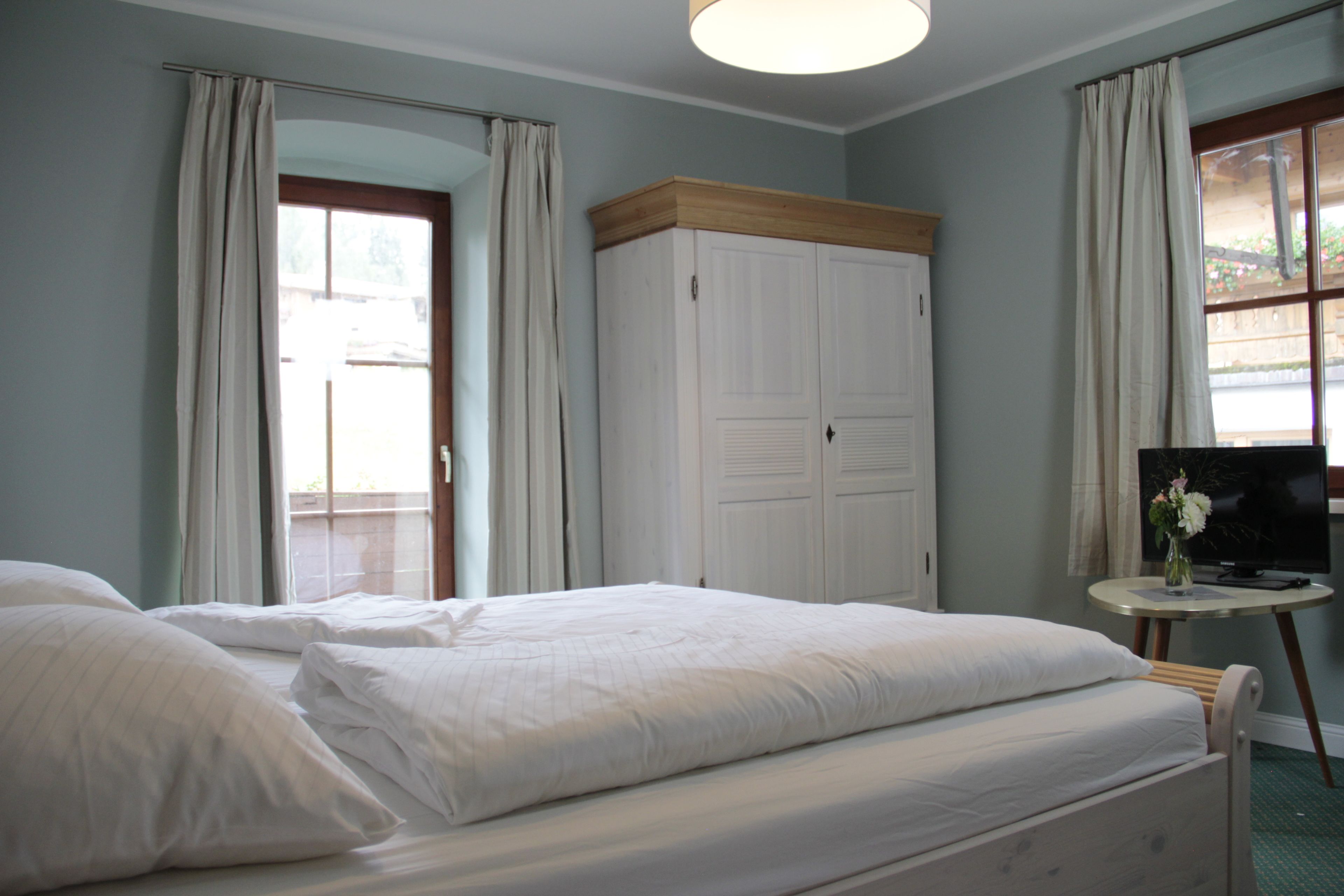A hotel room with two beds, a wardrobe, a television on a small table, and a window with curtains.