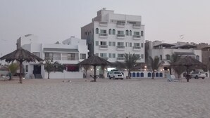 Ett hotell vid stranden med flera balkonger, palmer och parasoller med halmtak.