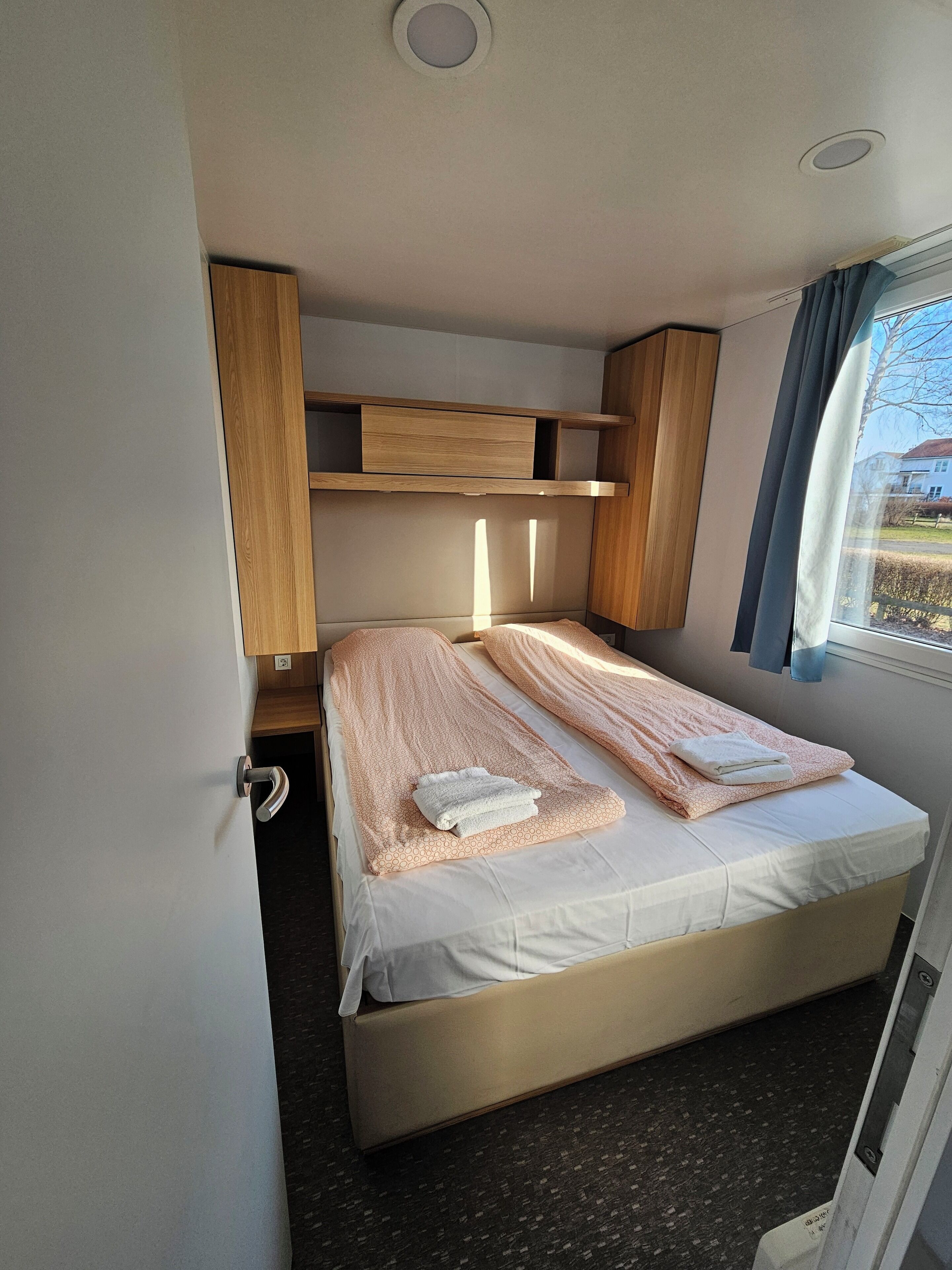 A compact bedroom with a bed, wooden headboard, and a window with curtains.