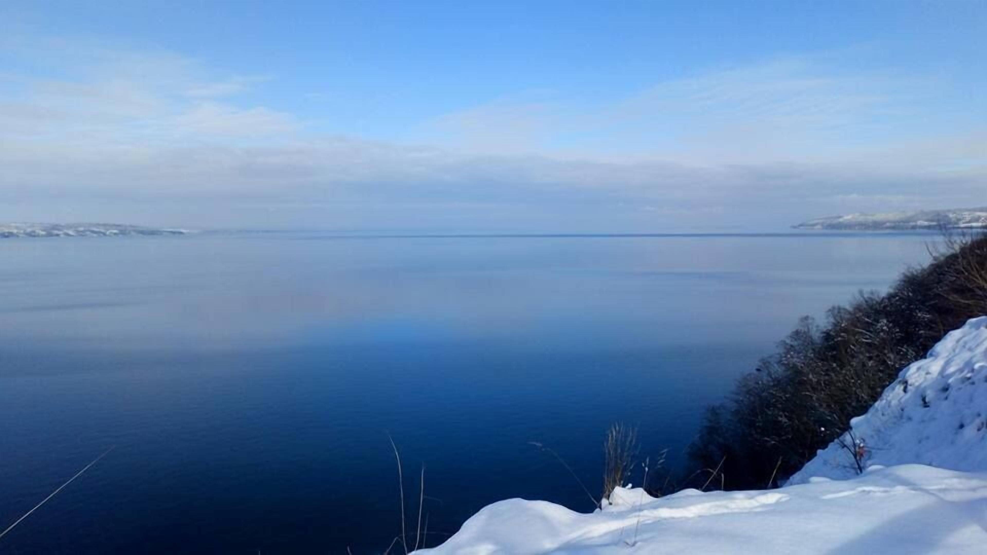 A serene lake with snow-covered terrain and distant landforms.