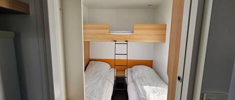 A compact room with bunk beds, a small shelf, and a ceiling light.