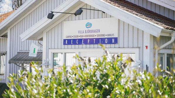 Un edificio con un cartel que dice "Villa Björkhagen Reception" y una lista de servicios que incluye camping, cabañas, habitaciones, conferencias, servicio de comidas y una tienda de ultramarinos.