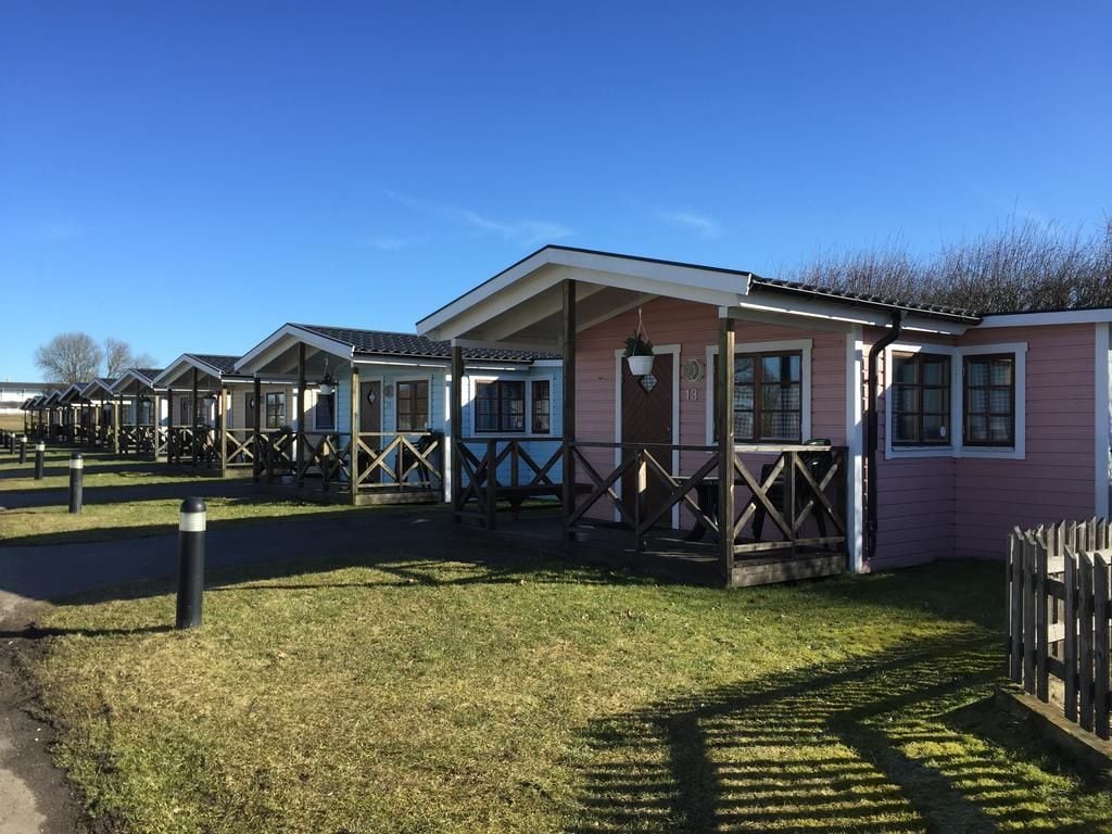 A row of pink mobile homes with wooden balconies, a paved walkway, and a grassy area.
