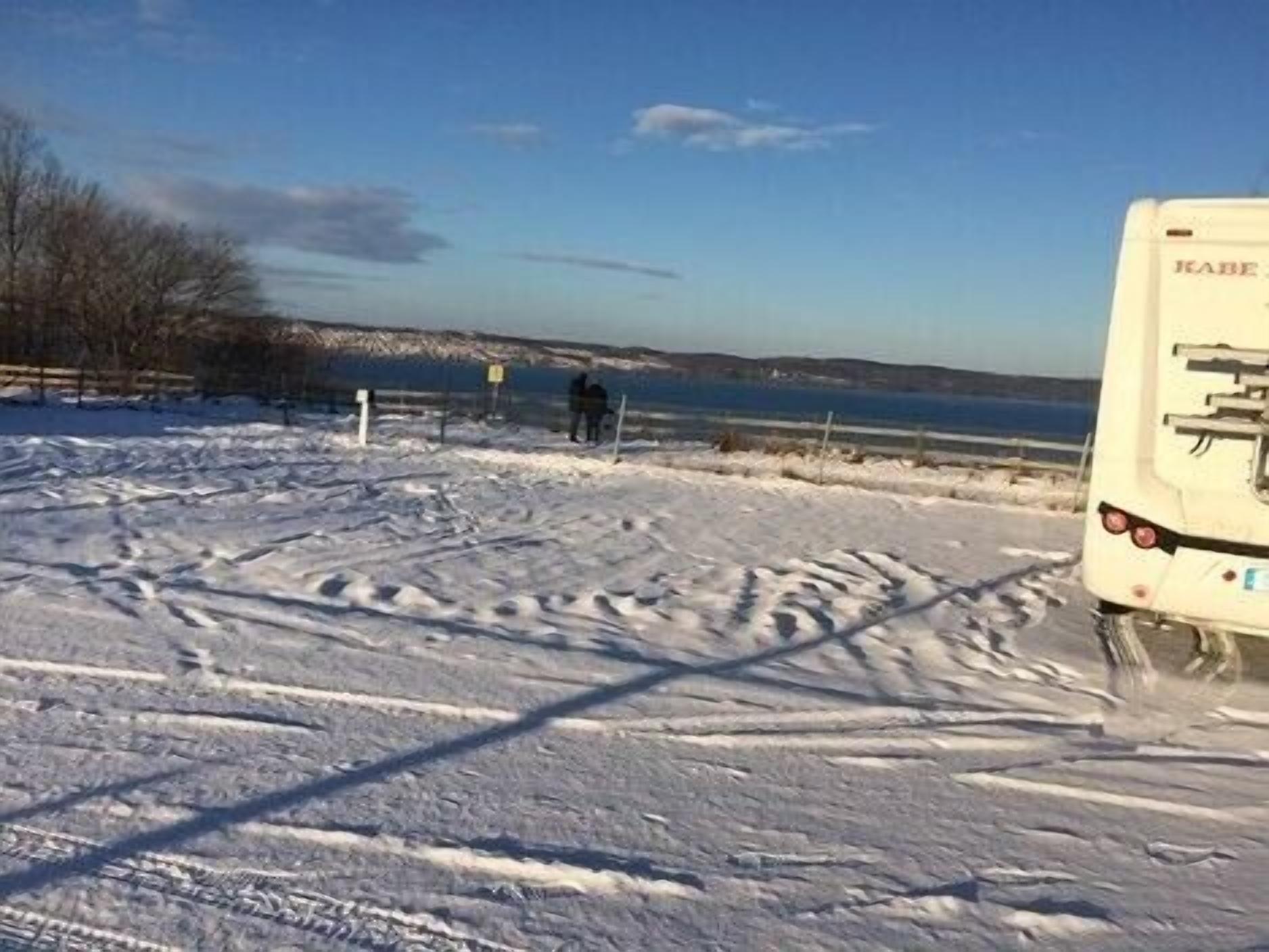 A snow-covered landscape with a white RV parked on the side of a road.