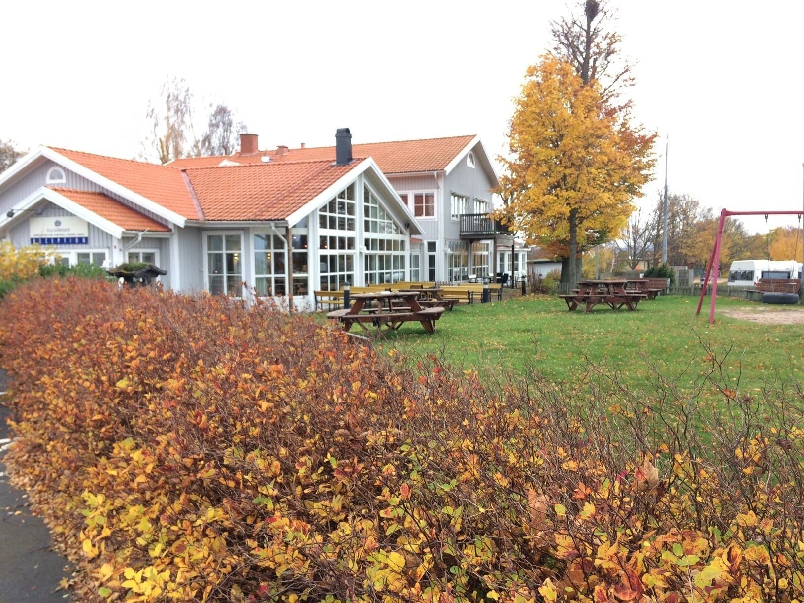 A building with a red-tiled roof, large windows, and a grassy area with picnic tables.