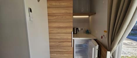 A compact kitchenette with a built-in refrigerator, a coffee maker, and a kettle on the countertop.