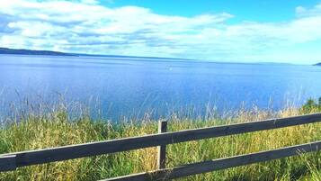 A wooden fence in the foreground with a view of a calm body of water and a clear sky in the background.
