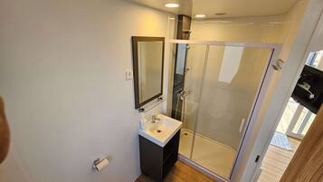 Un baño moderno con cabina de ducha de vidrio, un lavabo blanco y un espejo encima.