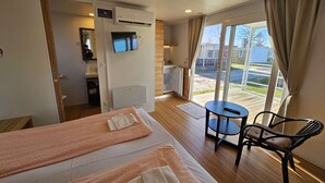 Habitación de hotel con dos camas, televisión, aire acondicionado, una pequeña mesa con silla y vista al exterior.
