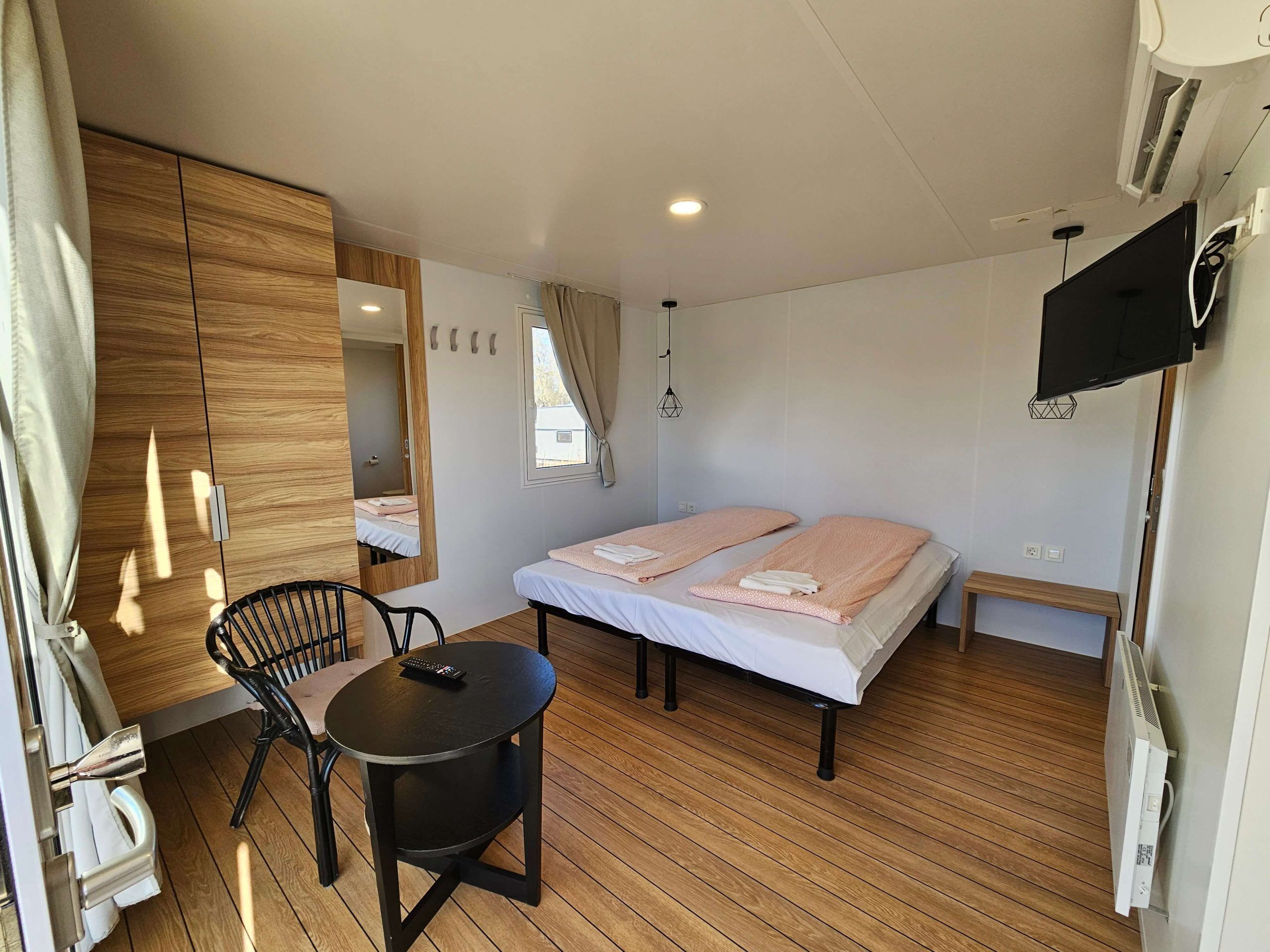 A room with two beds, a small table, a chair, a TV, and a wardrobe.