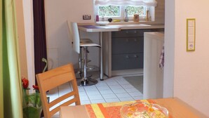 Una cocina compacta con comedor, con una mesa con mantel estampado, una silla y un jarrón con flores.