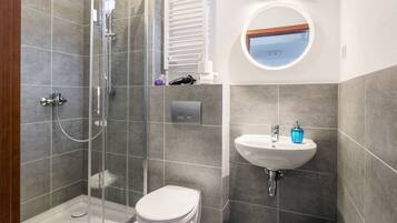 A modern bathroom with a glass-enclosed shower, a white toilet, a sink with a blue soap dispenser, and a mirror with a wooden frame.