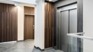 A modern elevator with a metallic finish, adjacent to a wooden-paneled corridor with a glass railing. - Green Garden Residence (Kraków)