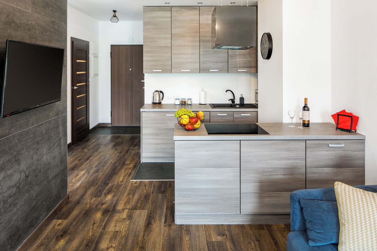 A modern kitchen with a built-in island, stainless steel appliances, and a flat-screen TV mounted on the wall.