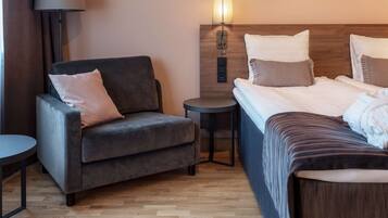 Une chambre d’hôtel avec un canapé, une petite table ronde, un lit avec une tête de lit en bois et une lampe fixée au mur.