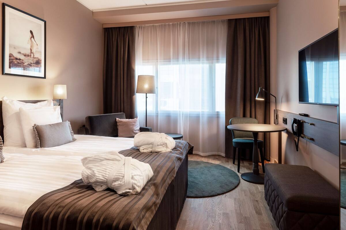 A hotel room with a large bed, a desk, a chair, a TV, and a window with curtains.