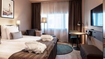A hotel room with a large bed, a desk, a chair, a TV, and a window with curtains.
