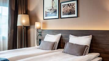 Habitación de hotel con dos camas, una mesita de noche, una lámpara y dos cuadros en la pared.