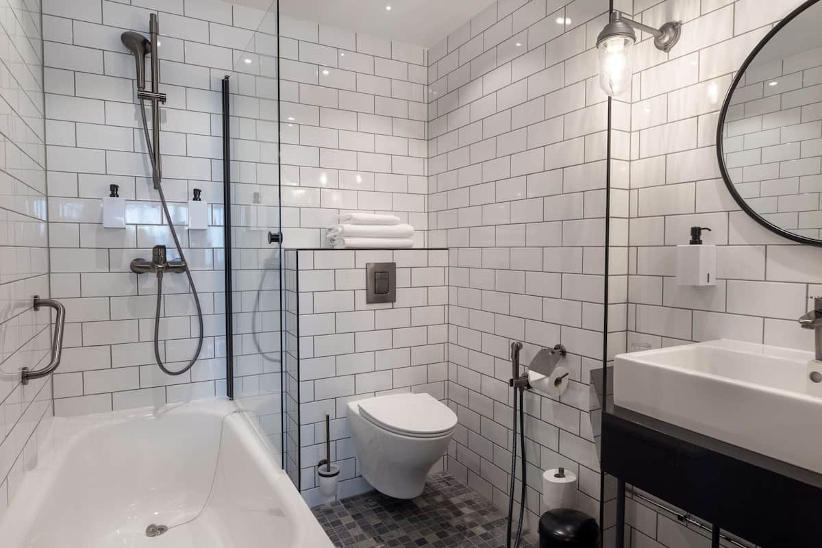 A modern bathroom with a bathtub, toilet, and sink, featuring white tiled walls and a glass shower enclosure.