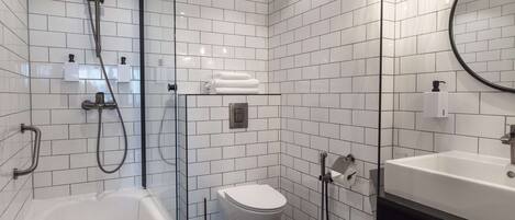 A modern bathroom with a bathtub, toilet, and sink, featuring white tiled walls and a glass shower enclosure.