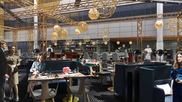 A modern restaurant with high ceilings, geometric chandeliers, and a bar area.