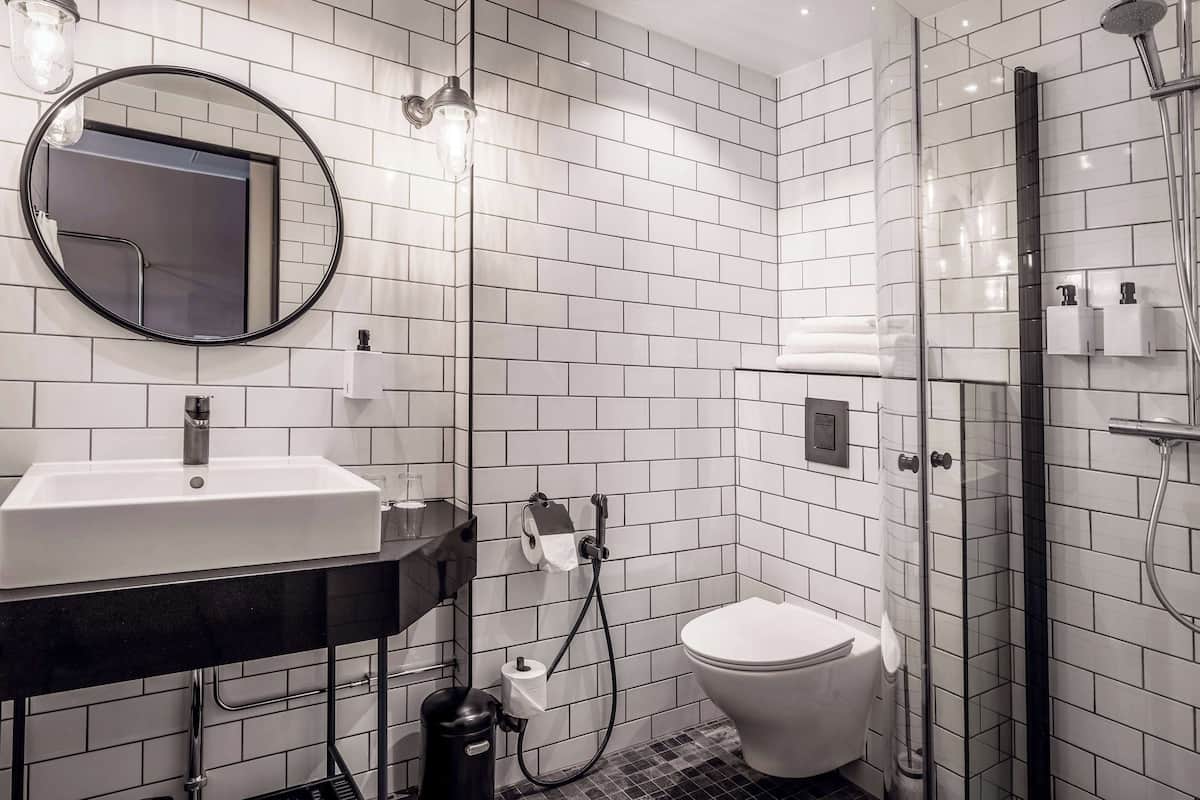 A modern bathroom with white subway tiles, a round mirror, a black sink, a toilet, and a glass-enclosed shower.