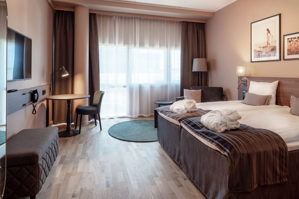 Hotellihuone, jossa on sänky, yöpöytä, tuoli, työpöytä ja puhelin.