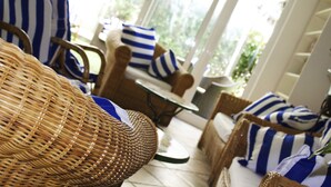 Muebles de mimbre con cojines a rayas azules y blancas, una mesa redonda y vistas a zonas verdes.